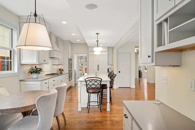 kitchen with a kitchen bar, a center island with sink, stainless steel appliances, white cabinets, and dark wood-type flooring
