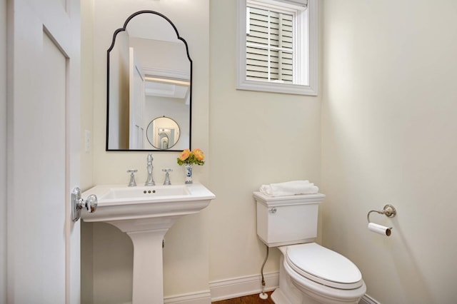 half bath featuring toilet, a sink, and baseboards