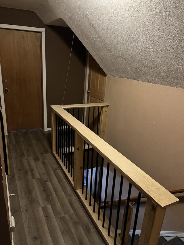 interior space featuring a textured ceiling, vaulted ceiling, wood finished floors, and baseboards