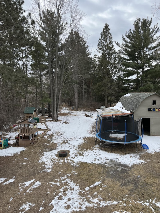 yard covered in snow with an outbuilding, a trampoline, and a playground