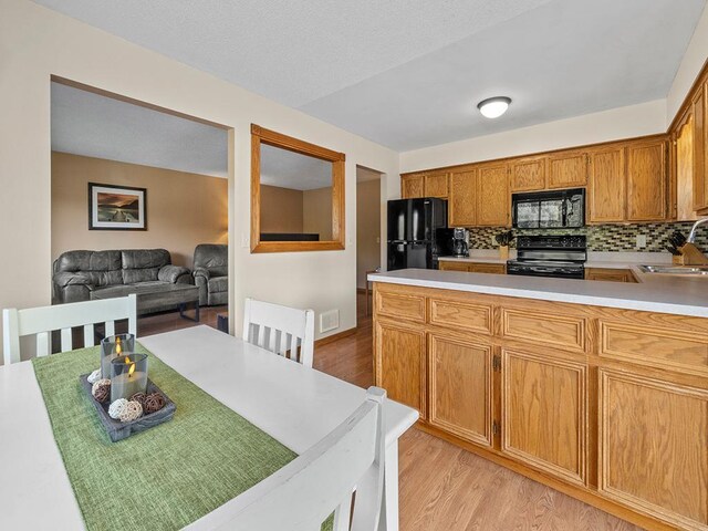 15029 Tyacke Dr, Burnsville, MN 55306 - kitchen with decorative backsplash, light countertops, light wood-style flooring, a sink, and black appliances