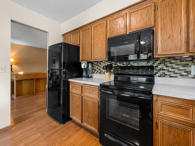 15029 Tyacke Dr, Burnsville, MN 55306 - kitchen with light countertops, brown cabinets, black appliances, light wood-style floors, and decorative backsplash