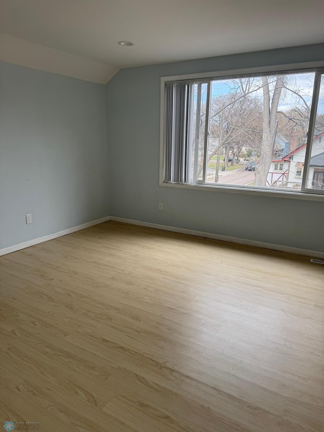 spare room featuring vaulted ceiling, a healthy amount of sunlight, and wood finished floors