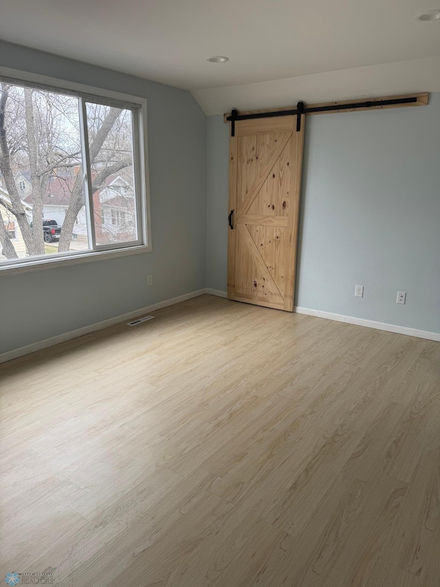 unfurnished room featuring a barn door, baseboards, visible vents, light wood-style floors, and lofted ceiling