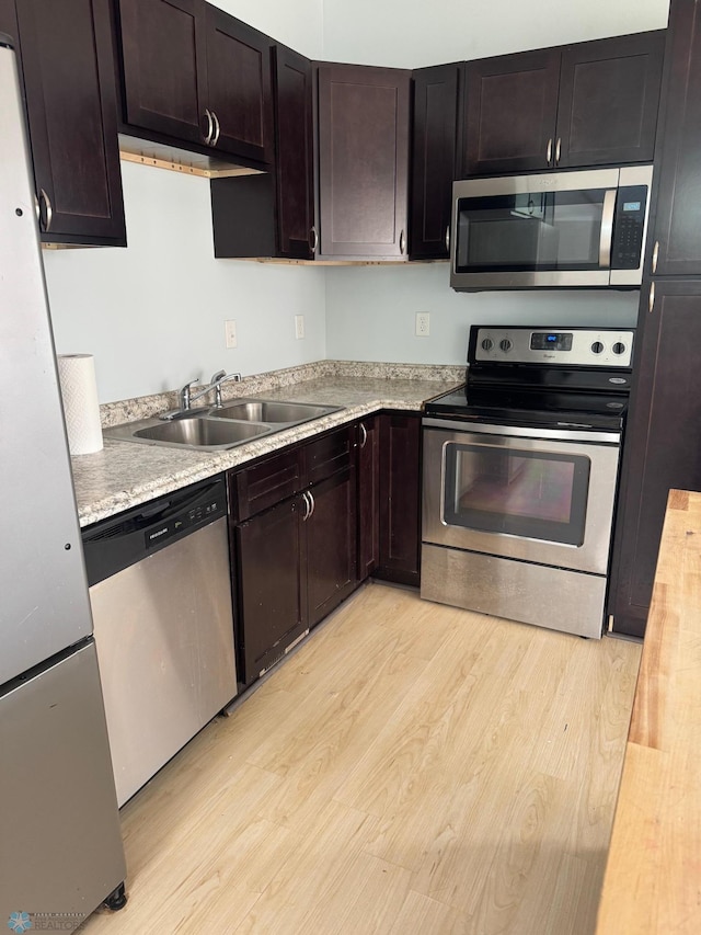 kitchen with dark brown cabinets, a sink, light wood finished floors, light countertops, and appliances with stainless steel finishes