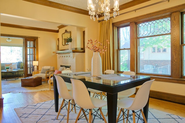 dining space featuring ornamental molding, hardwood / wood-style floors, a brick fireplace, and a chandelier