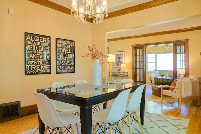 dining area with light wood-style floors, a chandelier, and ornamental molding