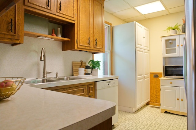 kitchen with stainless steel appliances, a sink, light floors, brown cabinets, and wainscoting