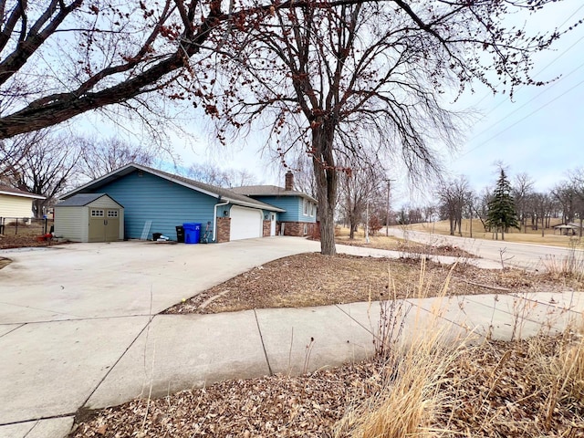 view of property exterior featuring an attached garage, a chimney, concrete driveway, brick siding, and an outdoor structure