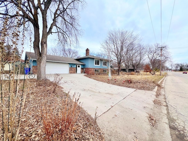 split level home featuring a chimney, a garage, brick siding, and driveway