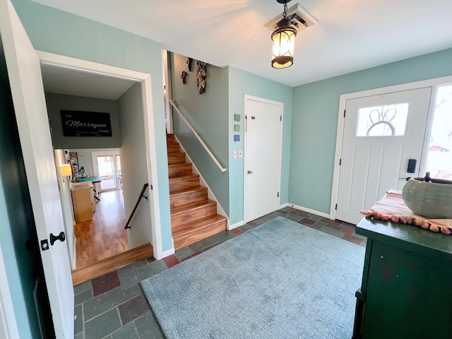foyer featuring baseboards, stairway, and stone tile floors
