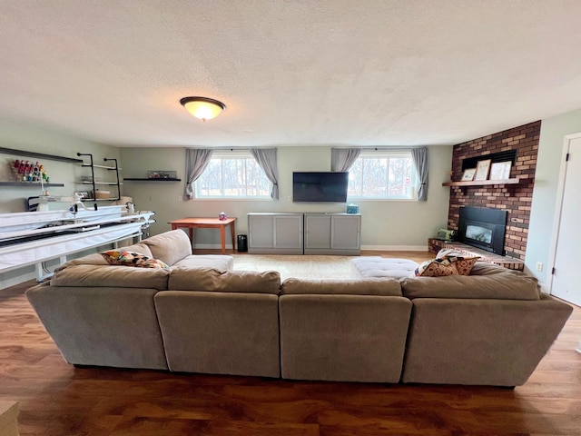 living room featuring a textured ceiling, wood finished floors, a brick fireplace, and plenty of natural light