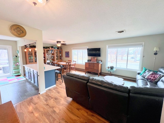 living room featuring a baseboard radiator, light wood-style flooring, visible vents, and a textured ceiling