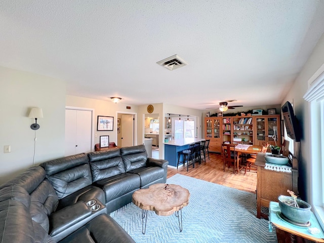 living area featuring visible vents, light wood-style floors, ceiling fan, and a textured ceiling