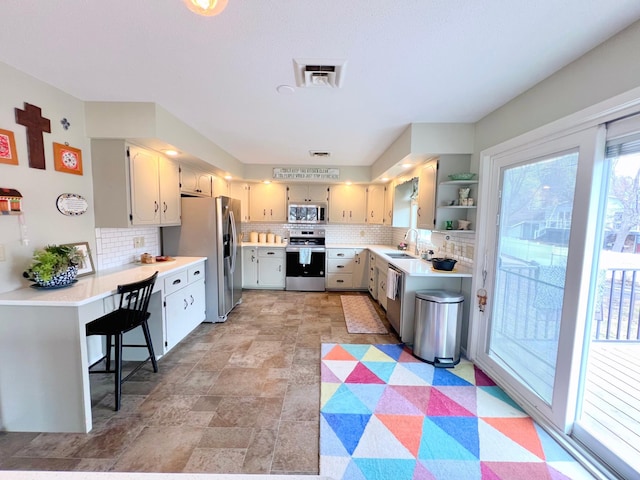 kitchen featuring light countertops, a sink, open shelves, appliances with stainless steel finishes, and decorative backsplash