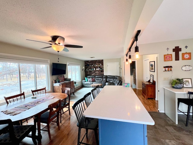 kitchen with light countertops, a breakfast bar, a textured ceiling, a kitchen island, and a ceiling fan