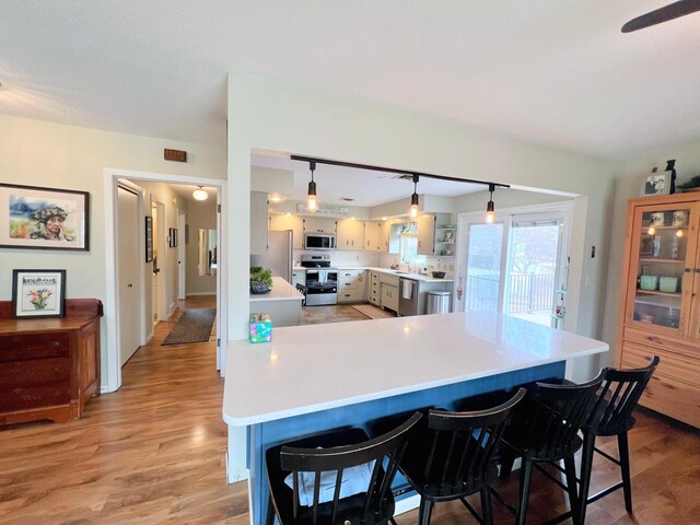 kitchen featuring a kitchen breakfast bar, light countertops, tasteful backsplash, light wood finished floors, and appliances with stainless steel finishes