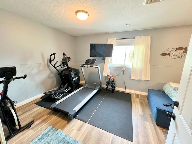 exercise room featuring a wainscoted wall, a textured ceiling, and wood finished floors