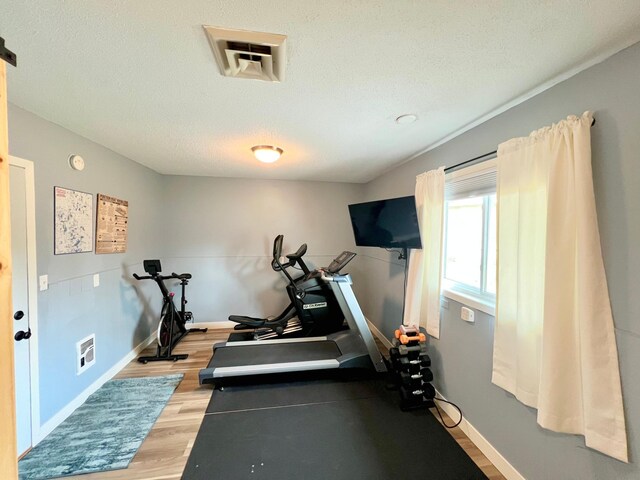exercise room featuring baseboards, a textured ceiling, and light wood-style floors