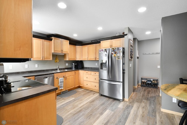 kitchen with light brown cabinetry, dark countertops, appliances with stainless steel finishes, and a sink