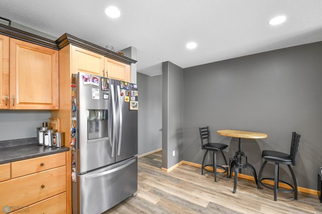 kitchen featuring light wood-style floors, dark countertops, light brown cabinetry, baseboards, and stainless steel fridge