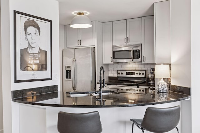kitchen with decorative backsplash, a sink, a peninsula, dark stone countertops, and stainless steel appliances