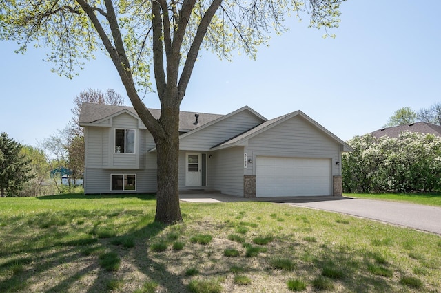 tri-level home with an attached garage, driveway, a front lawn, and roof with shingles