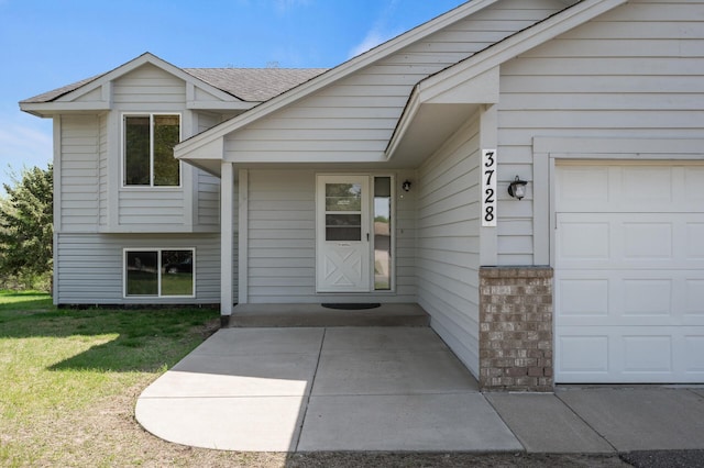 property entrance featuring brick siding, a lawn, an attached garage, and a shingled roof