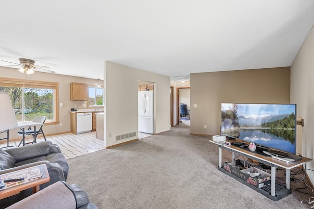 living area with ceiling fan, light carpet, and baseboards