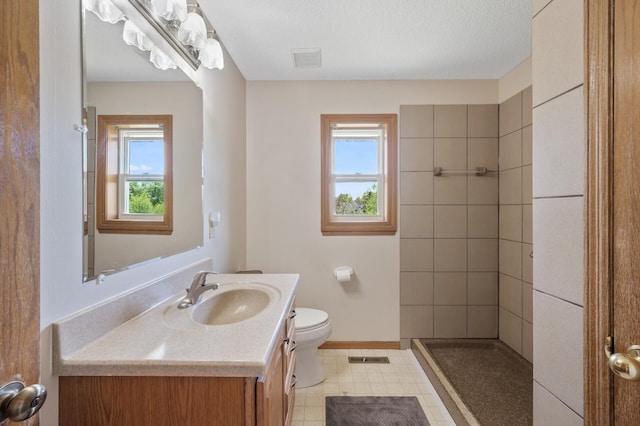 bathroom featuring healthy amount of natural light, vanity, toilet, and tiled shower