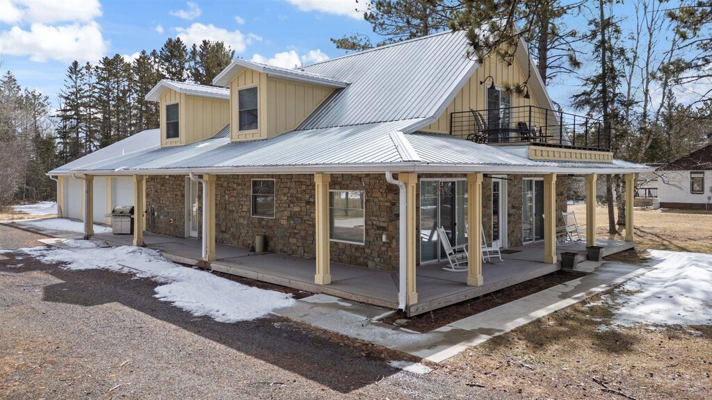7436 Ely Lake Dr, Eveleth, MN 55734 - back of house with covered porch, stone siding, a balcony, metal roof, and a garage