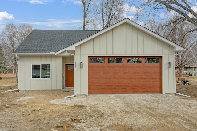 view of front of house featuring an attached garage, board and batten siding, an outdoor structure, a shingled roof, and dirt driveway