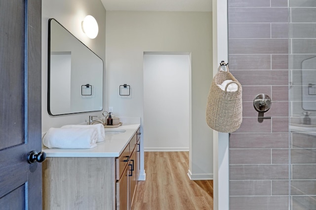 bathroom with tiled shower, vanity, baseboards, and wood finished floors