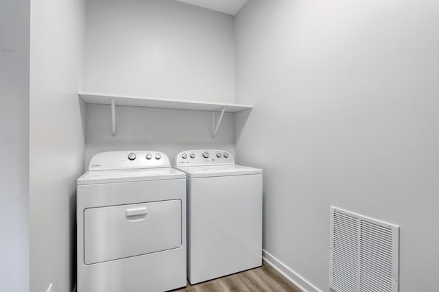 laundry room with baseboards, visible vents, washing machine and dryer, laundry area, and wood finished floors
