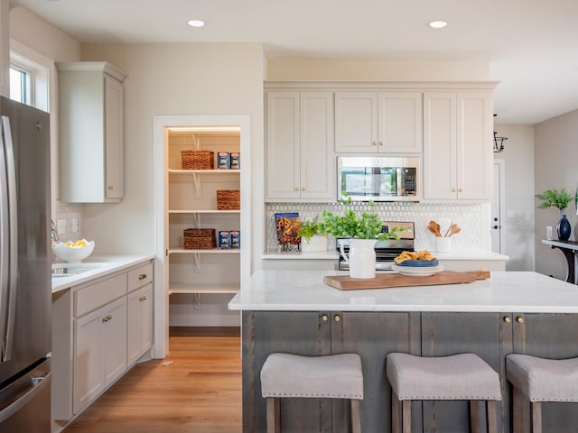 9160 62nd St S, Cottage Grove, MN 55016 - kitchen featuring appliances with stainless steel finishes, a kitchen breakfast bar, decorative backsplash, light countertops, and light wood-style floors