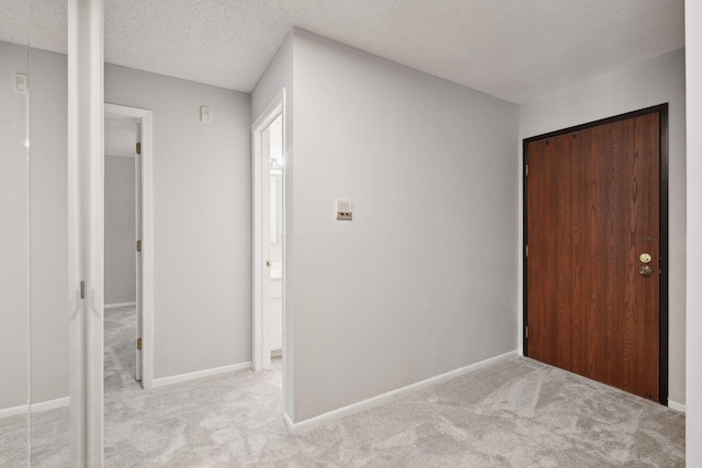 hallway featuring a textured ceiling, light colored carpet, and baseboards