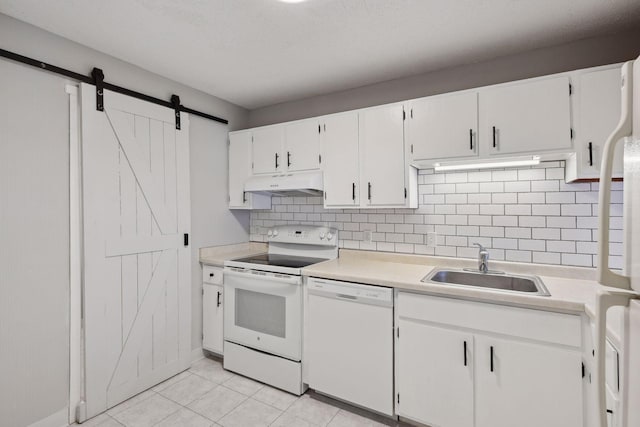 kitchen featuring white appliances, a barn door, under cabinet range hood, light countertops, and a sink