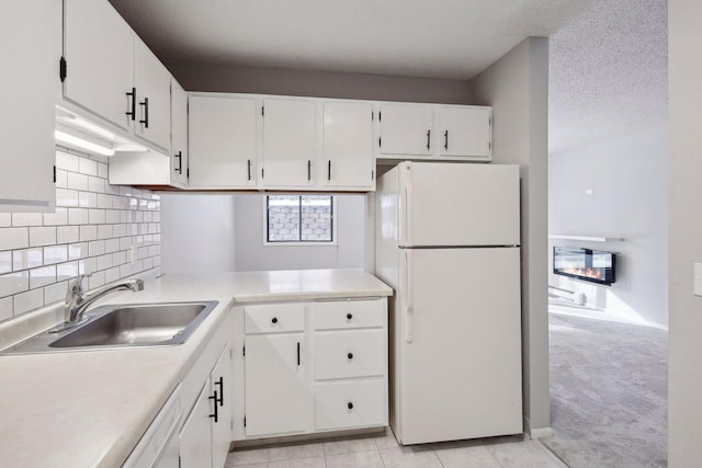 kitchen featuring white appliances, light colored carpet, white cabinets, light countertops, and a sink