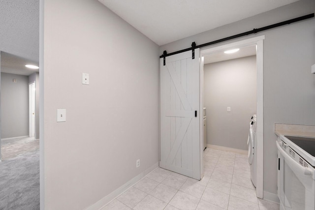 interior space with baseboards, light tile patterned floors, washing machine and dryer, a barn door, and white electric range oven