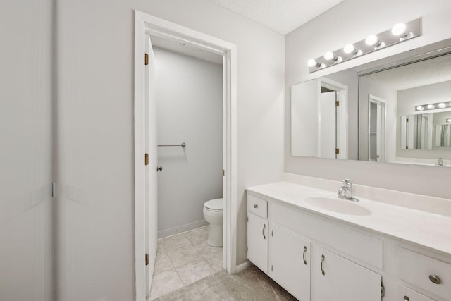 bathroom with vanity, a textured ceiling, baseboards, and toilet
