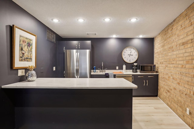 kitchen featuring brick wall, a peninsula, light wood-style flooring, a textured ceiling, and stainless steel appliances