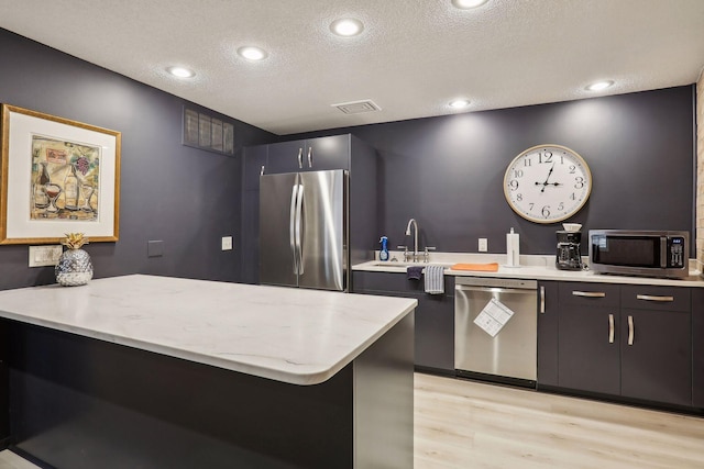 kitchen with visible vents, light wood-type flooring, appliances with stainless steel finishes, a peninsula, and a textured ceiling
