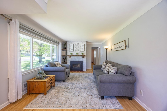 living area with light wood finished floors, a brick fireplace, and baseboards