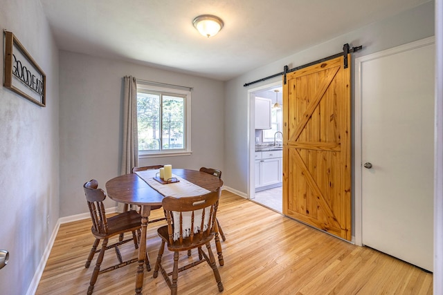 dining area with light wood-style floors, a barn door, and baseboards
