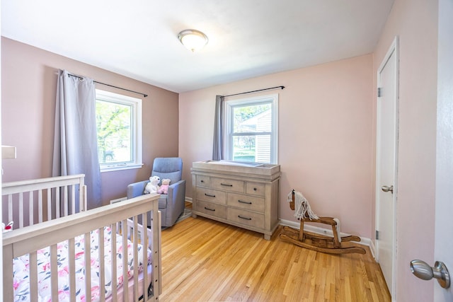 bedroom with multiple windows, light wood finished floors, a crib, and baseboards