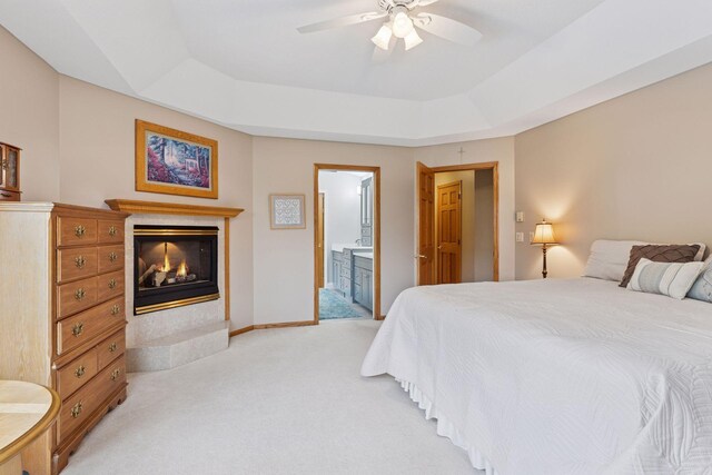 268 Saint Andrews Dr, Hudson, WI 54016 - bedroom featuring light colored carpet, a glass covered fireplace, a tray ceiling, connected bathroom, and a ceiling fan