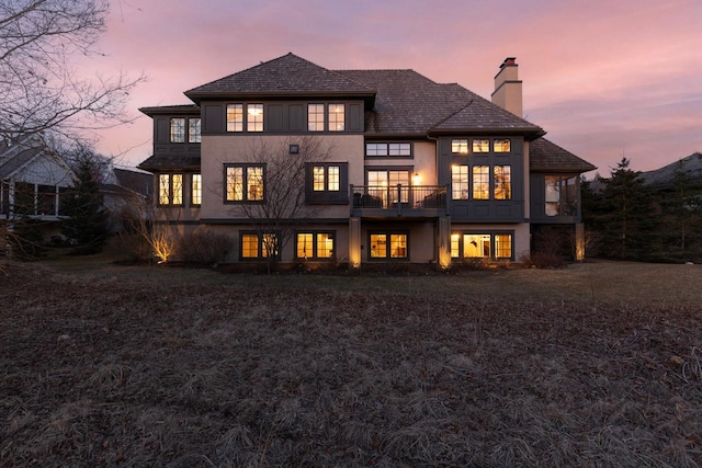 425 Carpenters Pt, Wayzata, MN 55391 - back of house at dusk featuring a chimney, stucco siding, and a balcony