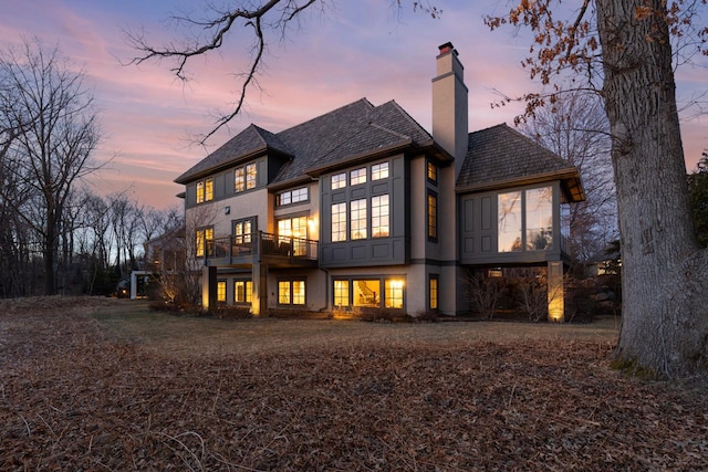 425 Carpenters Pt, Wayzata, MN 55391 - back of property at dusk featuring a balcony, a chimney, and stucco siding