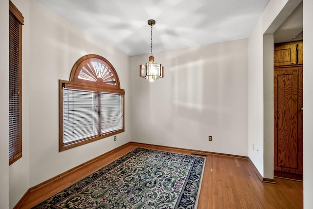 unfurnished dining area with baseboards, a notable chandelier, and light wood-style floors