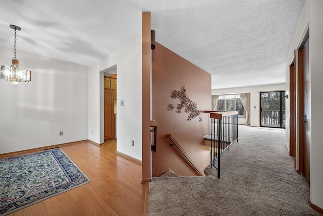 hall with light wood finished floors, baseboards, a textured ceiling, and an upstairs landing